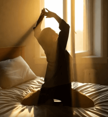 침대 옆 창문으로 햇살이 들어오는 이미지. 스트레칭 하는 사람의 실루엣 아침 3분 루틴하는 모습.